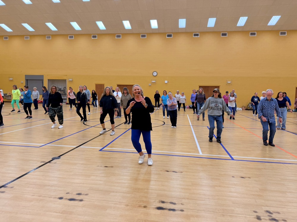 A group of people in a gymnasium doing a beginner line dancing class